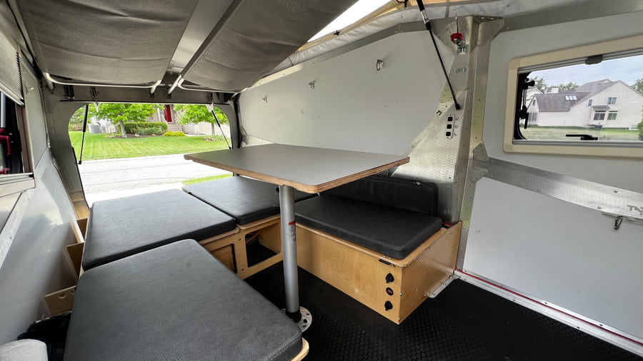 Inside a compact rv rental: a cozy dinette with dark cushions and a table, convertible to a sleeping area for comfortable travel.