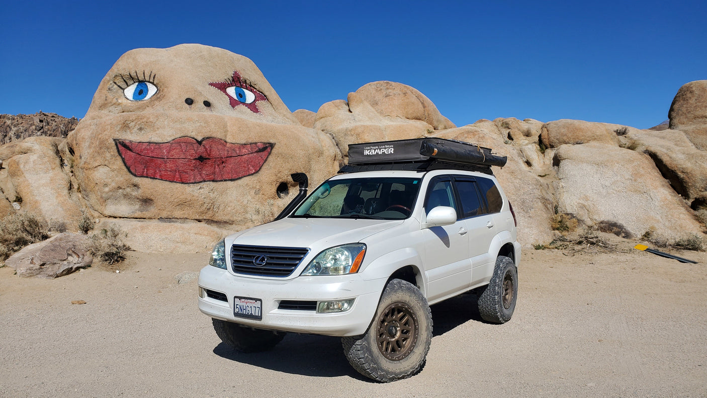 An off-road Lexus GX SUV with rooftop tent next to a painted rock face. Ideal for your next adventurous rv rental trip.