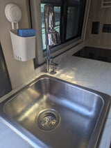 Clean RV rental kitchen featuring a stainless steel sink, chrome faucet, and a wall-mounted sponge holder with a blue sponge.