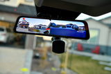 RV rental's smart rearview mirror shows split-screen live feeds of suburban homes, displaying time/date.