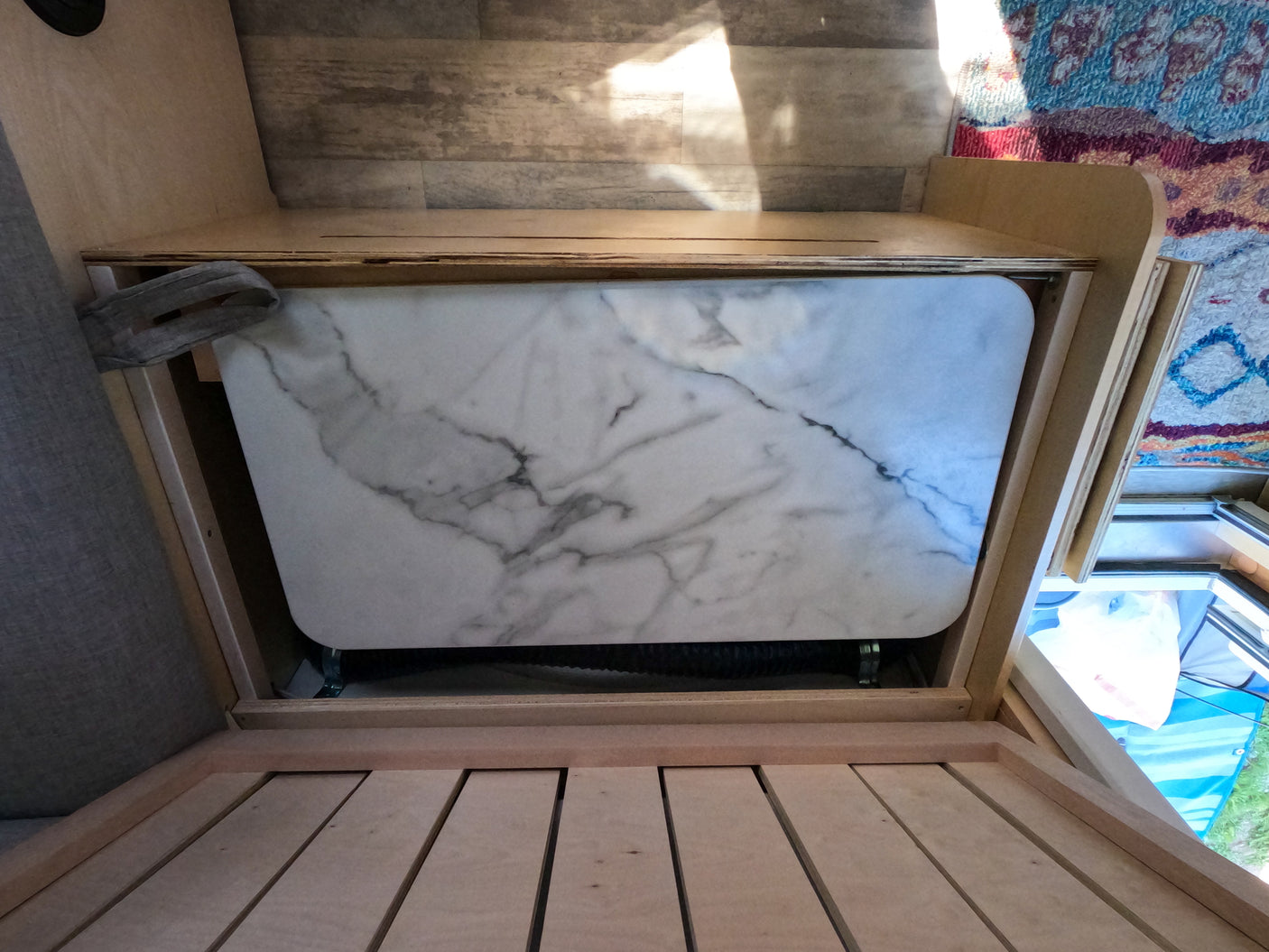 RV rental's functional interior: a white, marble-pattern table stores in a wooden cubby, with a slatted base in the foreground and a rug.