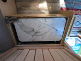 RV rental's functional interior: a white, marble-pattern table stores in a wooden cubby, with a slatted base in the foreground and a rug.