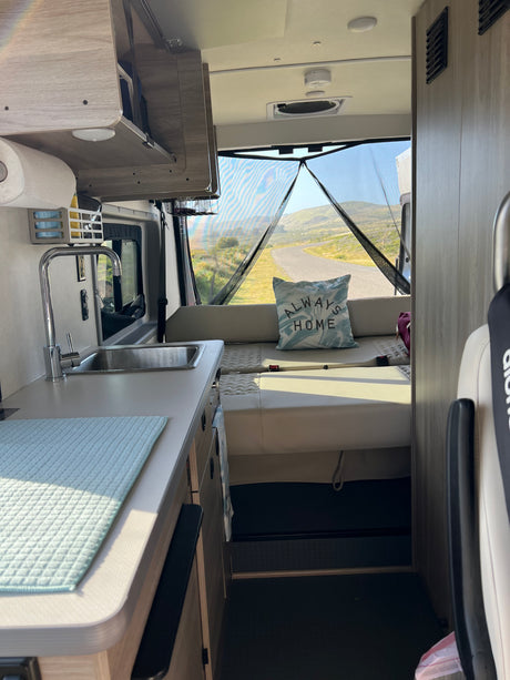 Cozy rv rental interior featuring a practical kitchenette, comfy seating, and a mesh-screened rear door opening to a scenic road.