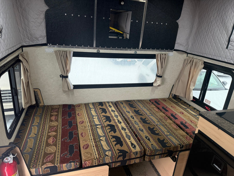 Explore this rv rental camper interior: comfy seats/bed with wilderness patterns, windows, and compact kitchenette. — photo 11