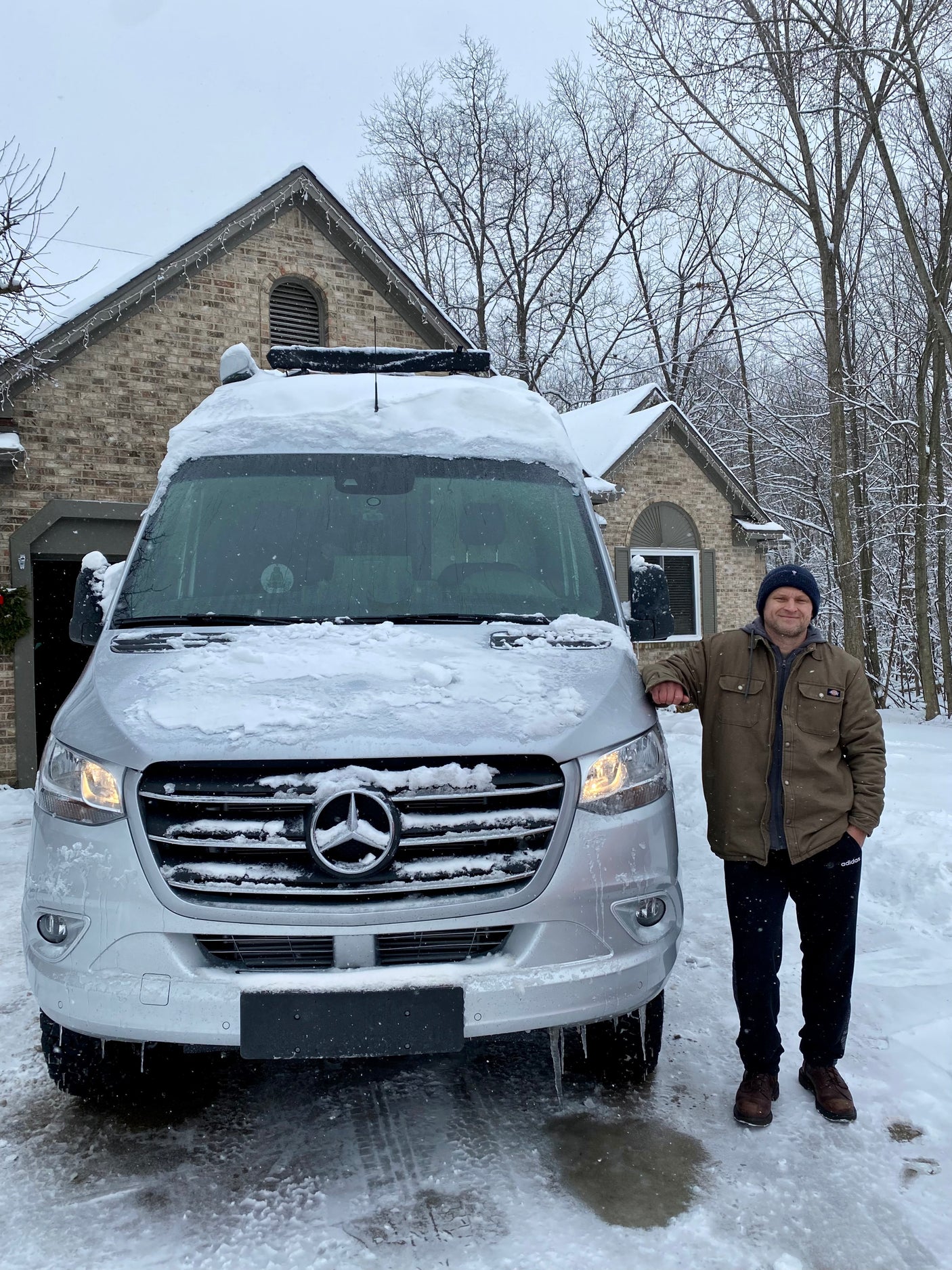 Man smiles next to his snow-covered Mercedes-Benz RV rental van, ready for winter travel adventures.