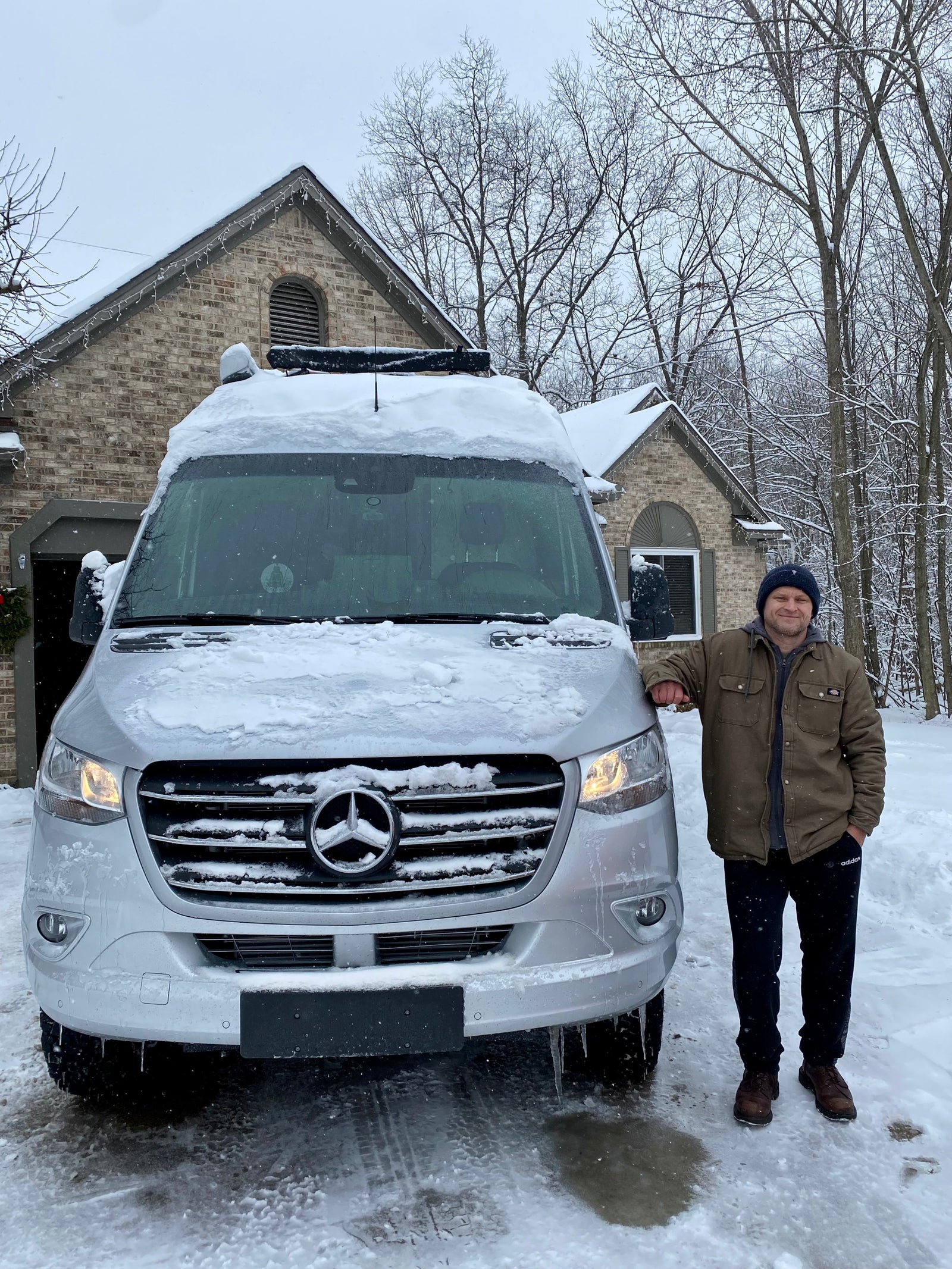 Man smiles next to his snow-covered Mercedes-Benz RV rental van, ready for winter travel adventures.