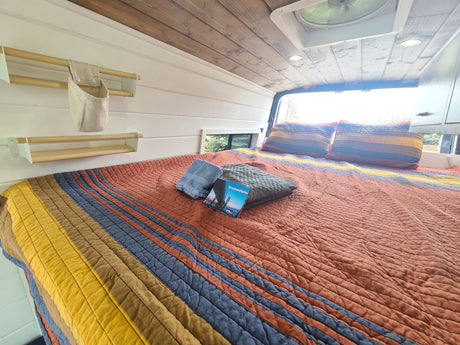 Step into comfort! This cozy RV rental features a colorful bed, wooden ceiling, and smart storage, ready for your next adventure.