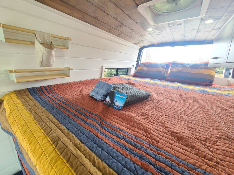 Step into comfort! This cozy RV rental features a colorful bed, wooden ceiling, and smart storage, ready for your next adventure.