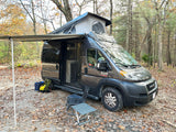 Grey Ram ProMaster RV rental with pop-top extended & awning out, parked in a scenic autumn forest campsite.