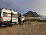 Scenic RV rental camping: a white van on a sandy beach with chairs, overlooking Morro Rock and the ocean.