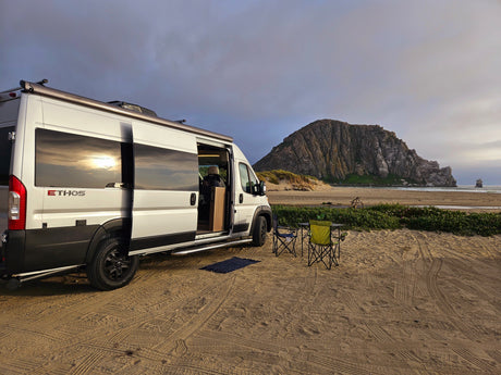 Scenic RV rental camping: a white van on a sandy beach with chairs, overlooking Morro Rock and the ocean.