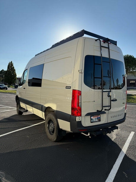 Light-colored Mercedes Sprinter camper van with roof rack, ladder, and AWD, parked outdoors. Perfect for rv rental adventures.