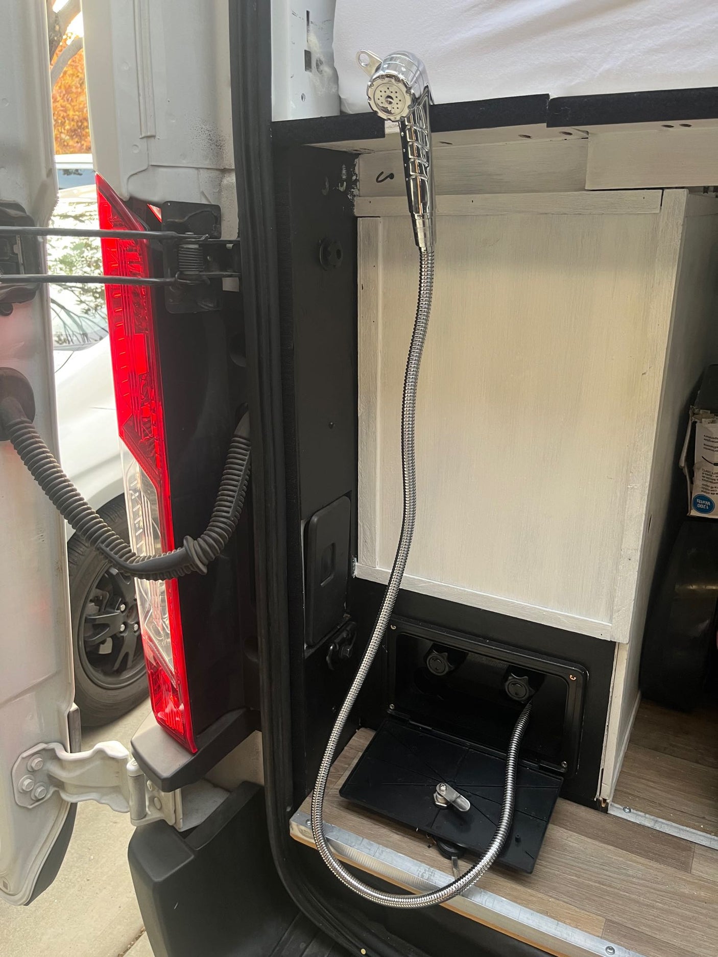 RV rental van's rear: Chrome pull-out shower head, hose, and water mixer panel for convenient outdoor use.