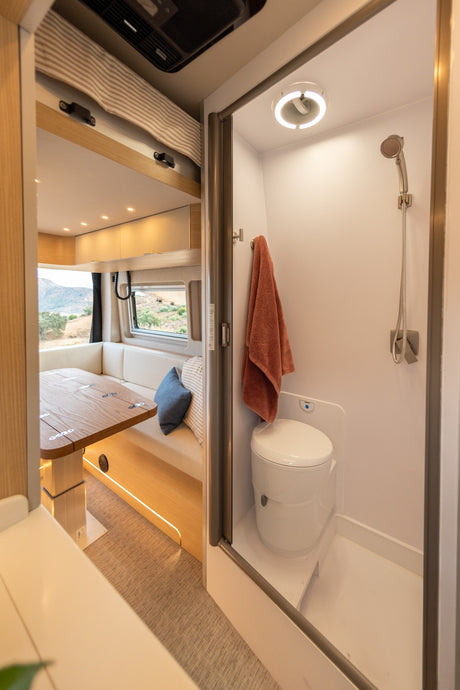 Inside an rv rental: A compact bathroom with toilet and shower, next to a dining area with a wooden table and window views.