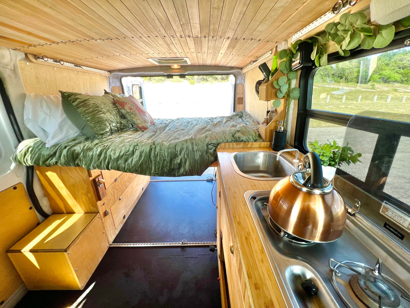 Stylish rv rental interior: wooden ceiling, cozy bed, and functional kitchen for your next van life adventure.