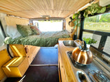 Stylish rv rental interior: wooden ceiling, cozy bed, and functional kitchen for your next van life adventure.