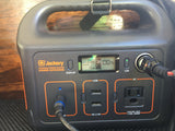 A Jackery portable power station, fully charged at 100%, powers devices, perfect for an RV rental or camping trip.