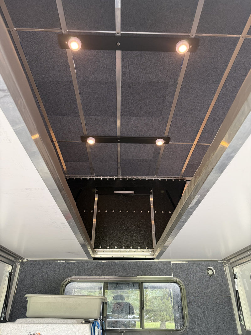 Looking up at the camper ceiling from inside, showing the carpeted insulated ceiling panels, aluminum cross ribs, two dual-LED light bars and the cabover section above the truck cab — photo 5