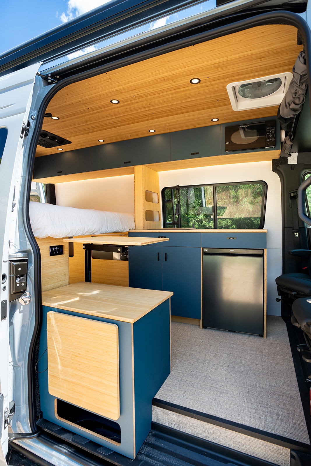 Modern rv rental camper van interior: compact kitchen, fold-out dining, comfortable bed, bamboo and blue accents. — photo 3