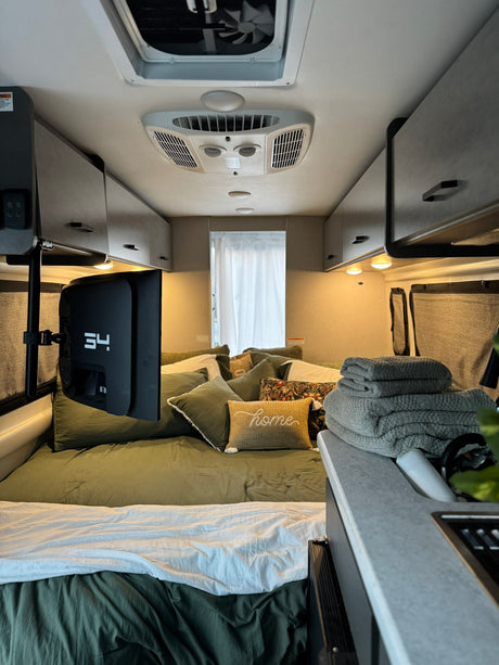 Experience comfort in this RV rental bedroom, featuring olive green bedding, a mounted TV, and convenient overhead storage.