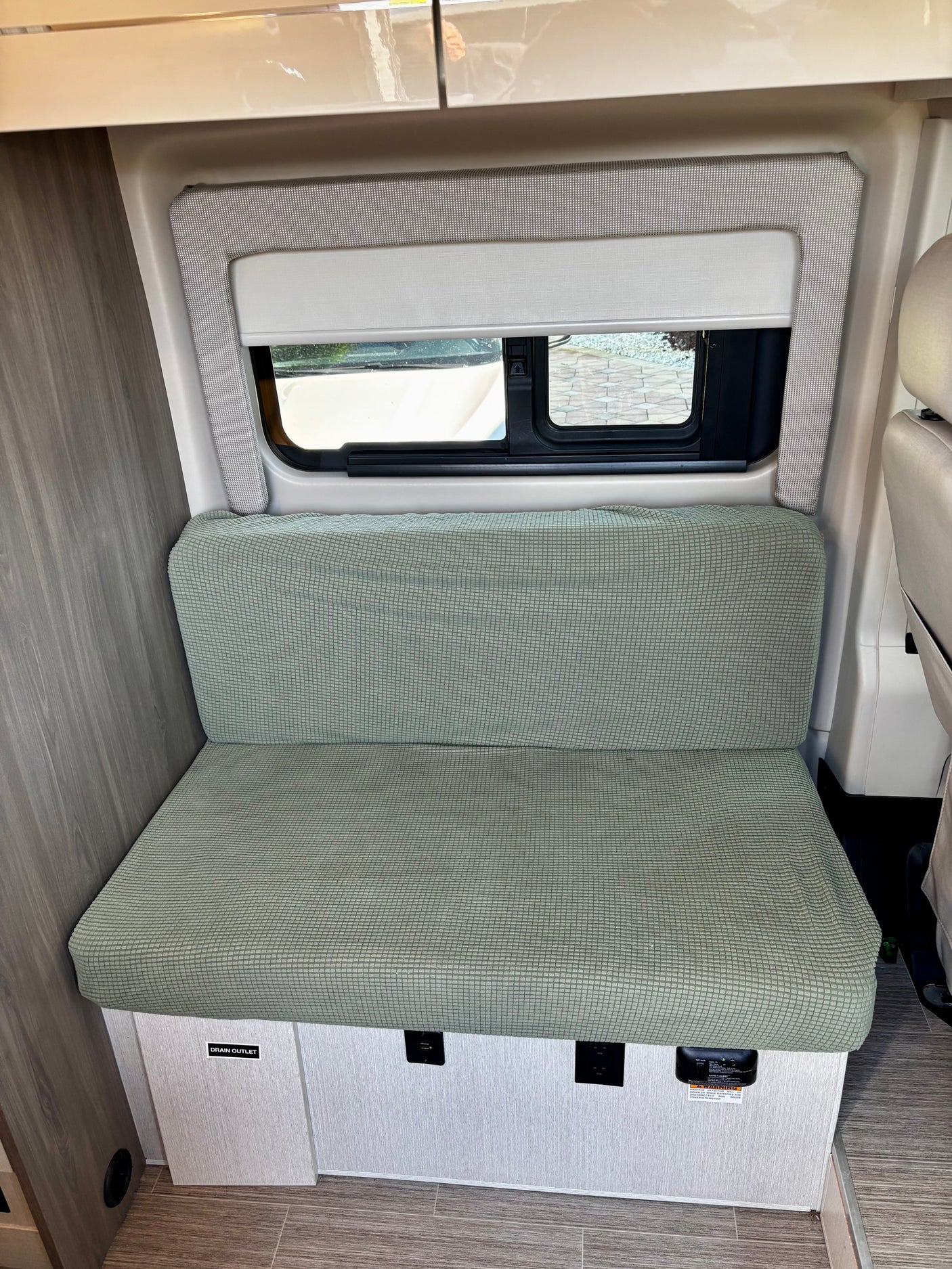 RV rental: Cozy light green bench seat, window, and outlets/detector in a modern camper van interior.