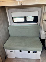 RV rental: Cozy light green bench seat, window, and outlets/detector in a modern camper van interior.