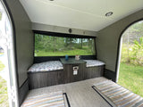 Interior of an RV rental featuring a cozy dinette with cushioned benches, a table, and a large window showcasing a forest view.