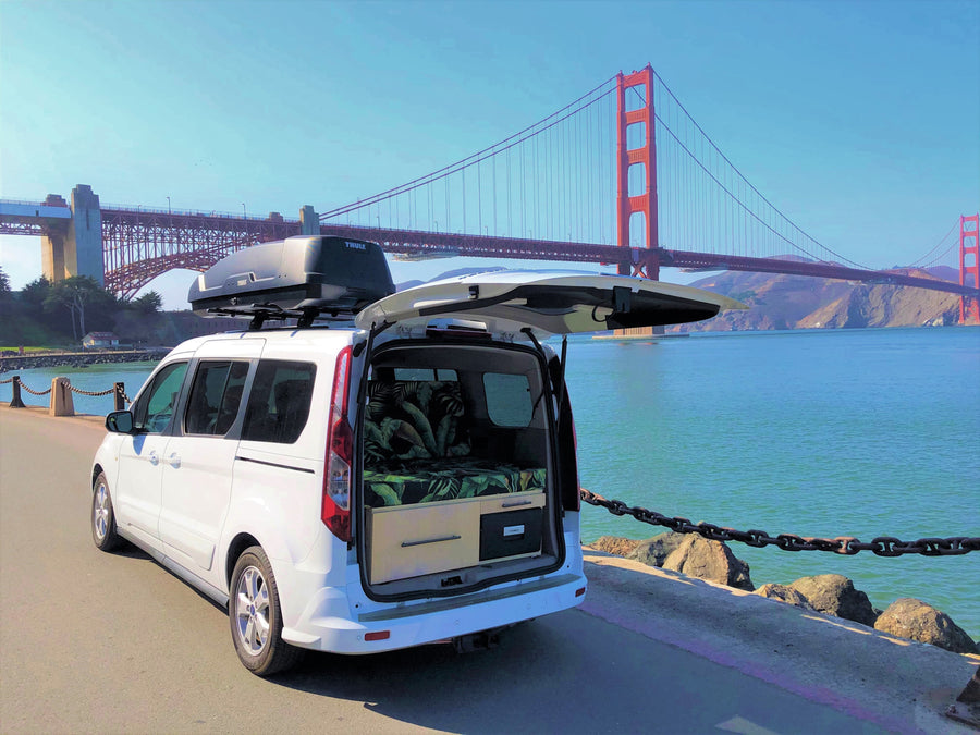 White campervan RV rental with Thule box by Golden Gate Bridge. Its open rear reveals a custom bed, ready for adventure.