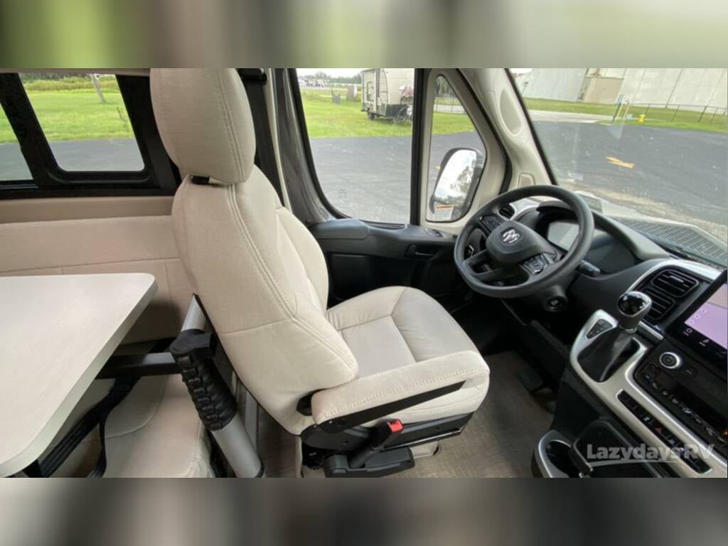 This RV rental's interior features a swiveled beige passenger seat, attached table, and the driver's cockpit with steering wheel.