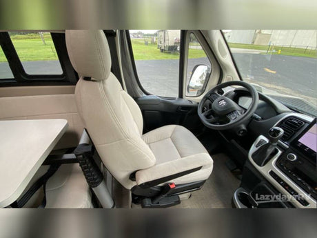 This RV rental's interior features a swiveled beige passenger seat, attached table, and the driver's cockpit with steering wheel.