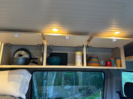 Organized RV rental interior showcasing open overhead cabinets with cookware, dishes, and cleaning supplies.