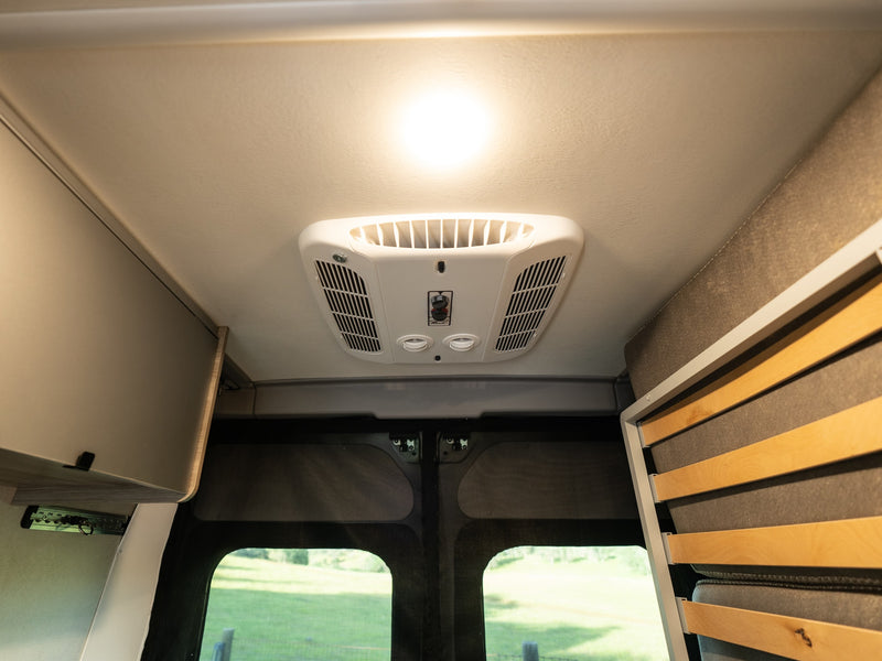 Stay cool in your RV rental with this ceiling-mounted air conditioner, bright light, and cozy interior details. — photo 16