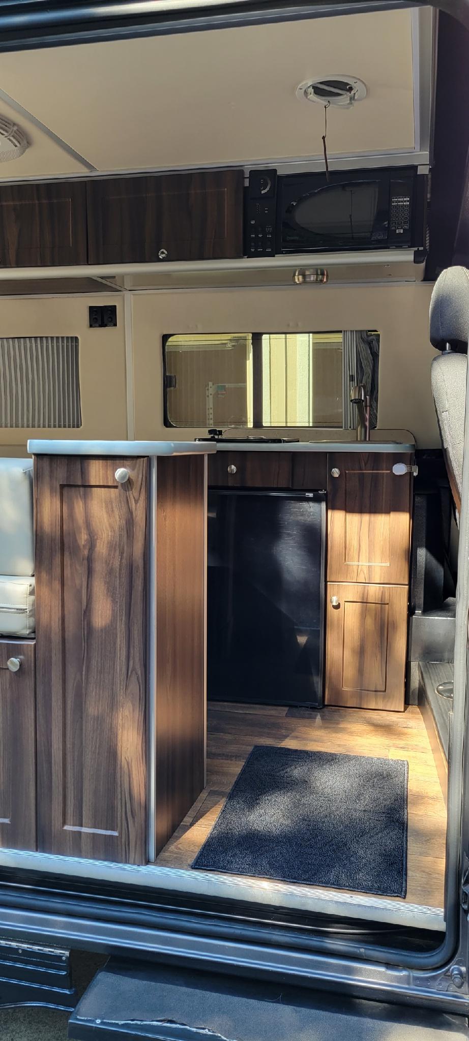 Modern RV rental interior: compact kitchen with sink, fridge, microwave, and wood-grain cabinets for comfortable travel. — photo 10