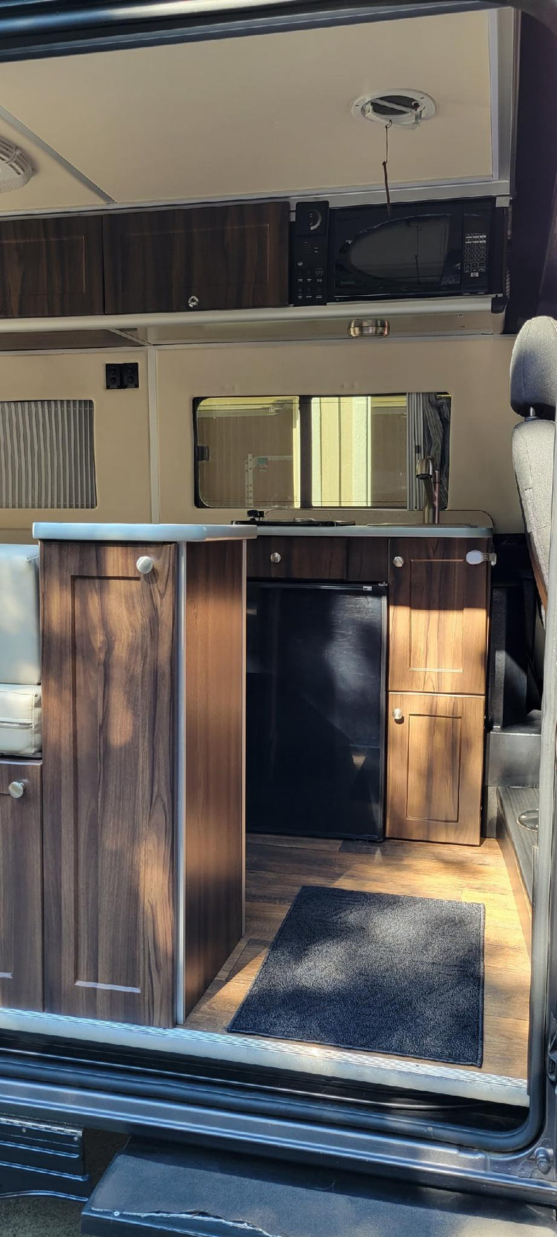 Modern RV rental interior: compact kitchen with sink, fridge, microwave, and wood-grain cabinets for comfortable travel. — photo 10