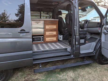 This RV rental features a well-designed custom interior, including a kitchen with a stainless steel fridge, microwave, and wood cabinets.