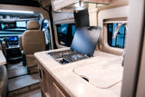 RV rental: Inside a camper van, showing a compact kitchen with a stove and sink in the foreground and the driver's cabin beyond.