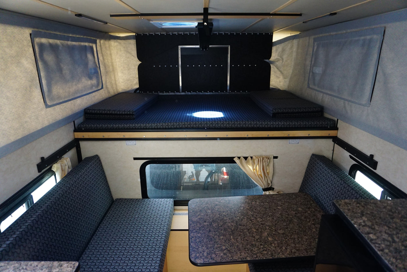  featuring an upper bed and lower dinette with seating and a table.|This rv rental interior features a compact pop-up camper's kitchen (sink — photo 4