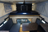 Inside a clean RV rental, featuring an upper bed and lower dinette with seating and a table.