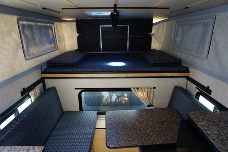 Inside a clean RV rental, featuring an upper bed and lower dinette with seating and a table.