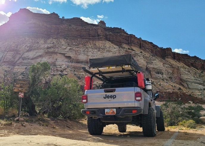This overland-equipped Jeep Gladiator, a unique RV rental alternative, awaits adventure in a vast desert canyon.