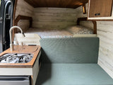 RV rental interior: A cozy camper van featuring a bed, kitchen with stove, and green seating area with wood walls.