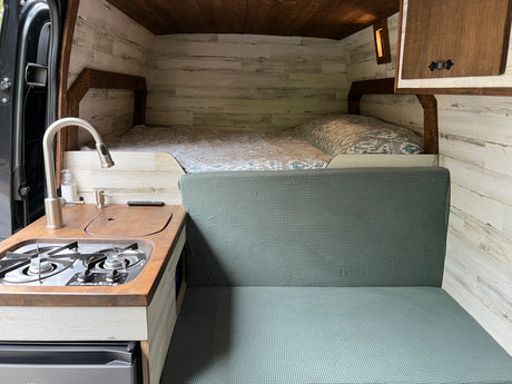 RV rental interior: A cozy camper van featuring a bed, kitchen with stove, and green seating area with wood walls.
