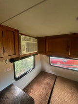 RV rental interior: window AC, wood cabinets, and cushioned benches. An 'EXIT' sign is near a window, with trees visible outside.