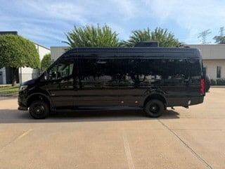 Sleek black Mercedes-Benz Sprinter van for RV rental. This luxury camper conversion is parked on a sunny paved lot.|Explore this luxury rv rental interior: dark wood paneling