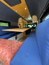 Spacious RV rental interior featuring a wooden dining table, blue upholstered benches, and custom cabinetry for comfort.