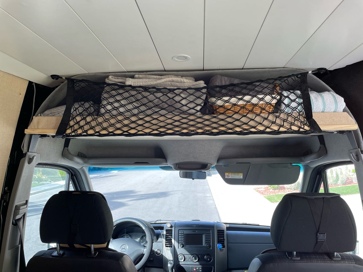 RV rental: Overhead storage in a Mercedes camper van. A black cargo net holds blankets and a basket above the front cabin. — photo 18