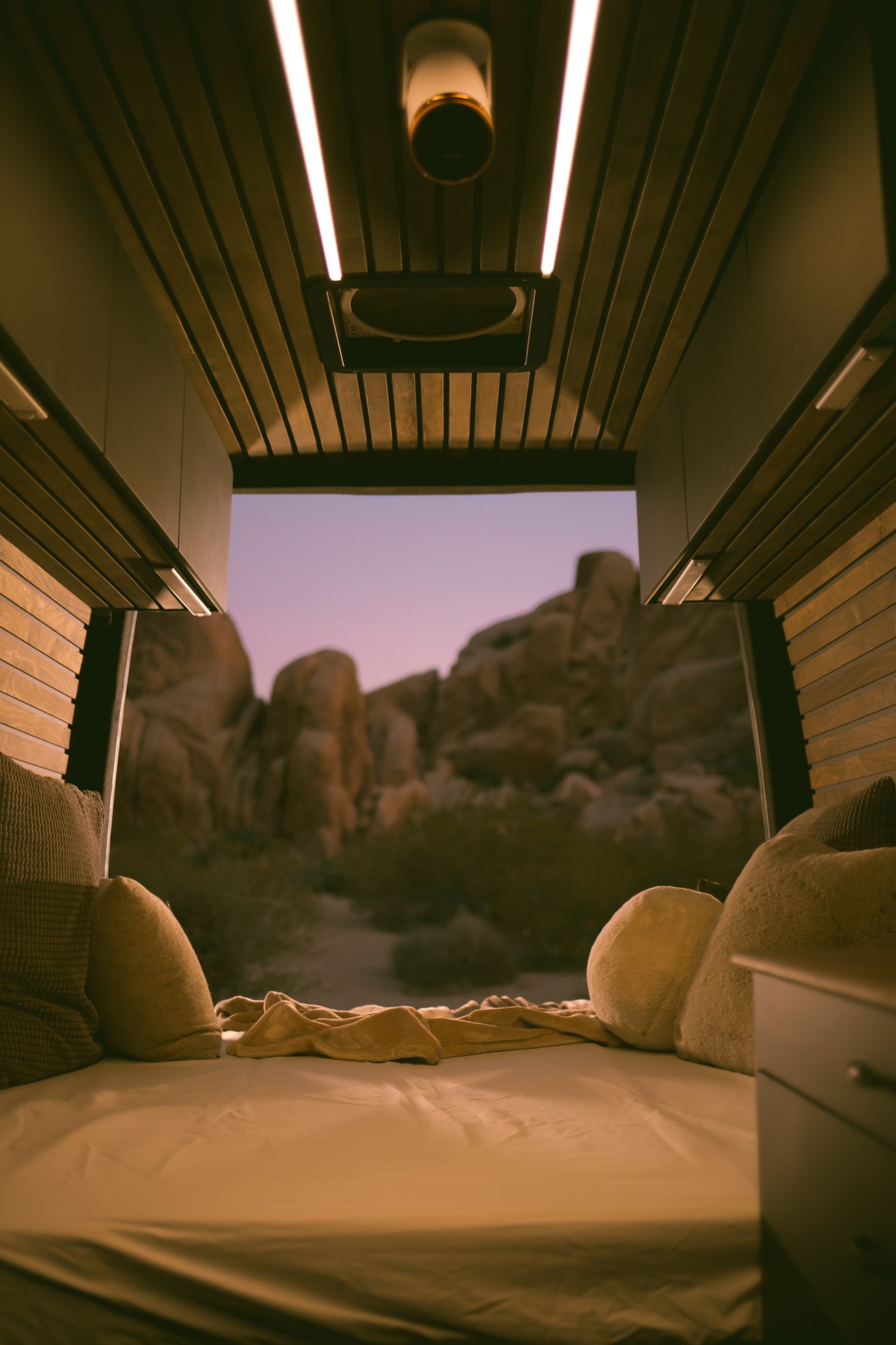 Cozy rv rental camper van interior with a comfortable bed and pillows, offering a stunning twilight desert view. Perfect for van life.