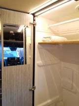 RV rental interior: Bright, compact wet bath featuring a mirrored cabinet door, shelf with towel, and shower area.
