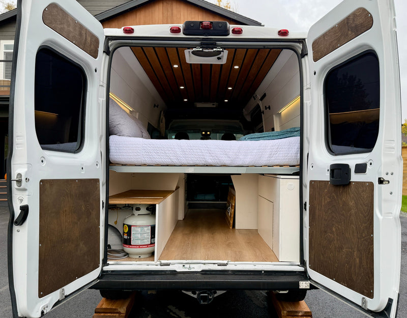 RV rental: Open rear of a white camper van conversion, showcasing its bed, wood-paneled interior, and under-bed storage. — photo 10