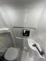 This RV rental's compact wet bath features a white toilet, corner sink with faucet, and chrome wall dispenser. Practical for camper travel.